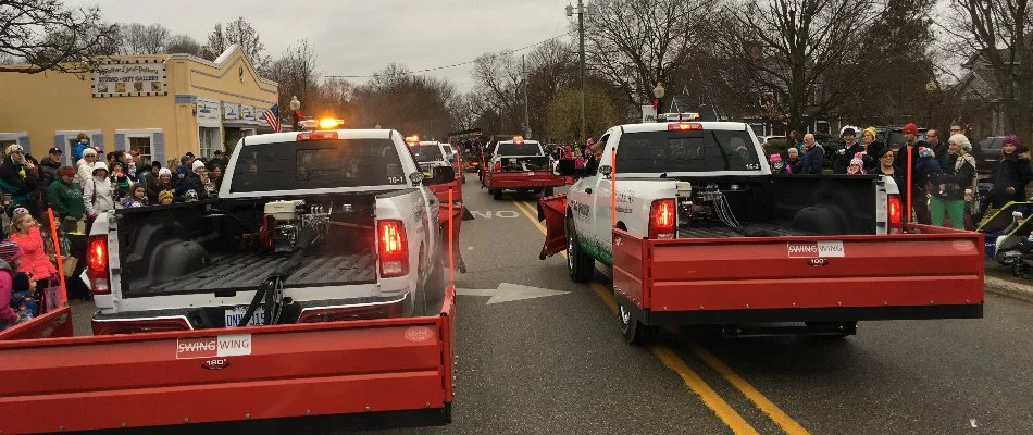 Pickup trucks with attached snow plows driving down a street during a parade in Ada, MI.