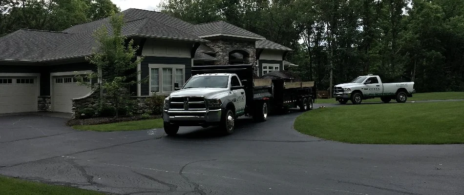 Two pickup trucks parked in the driveway of a modern house surrounded by trees in Ada, MI.