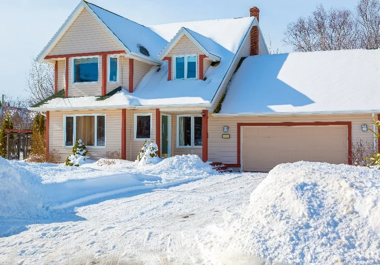 Home covered in snow with snowy driveway in Ada, MI.